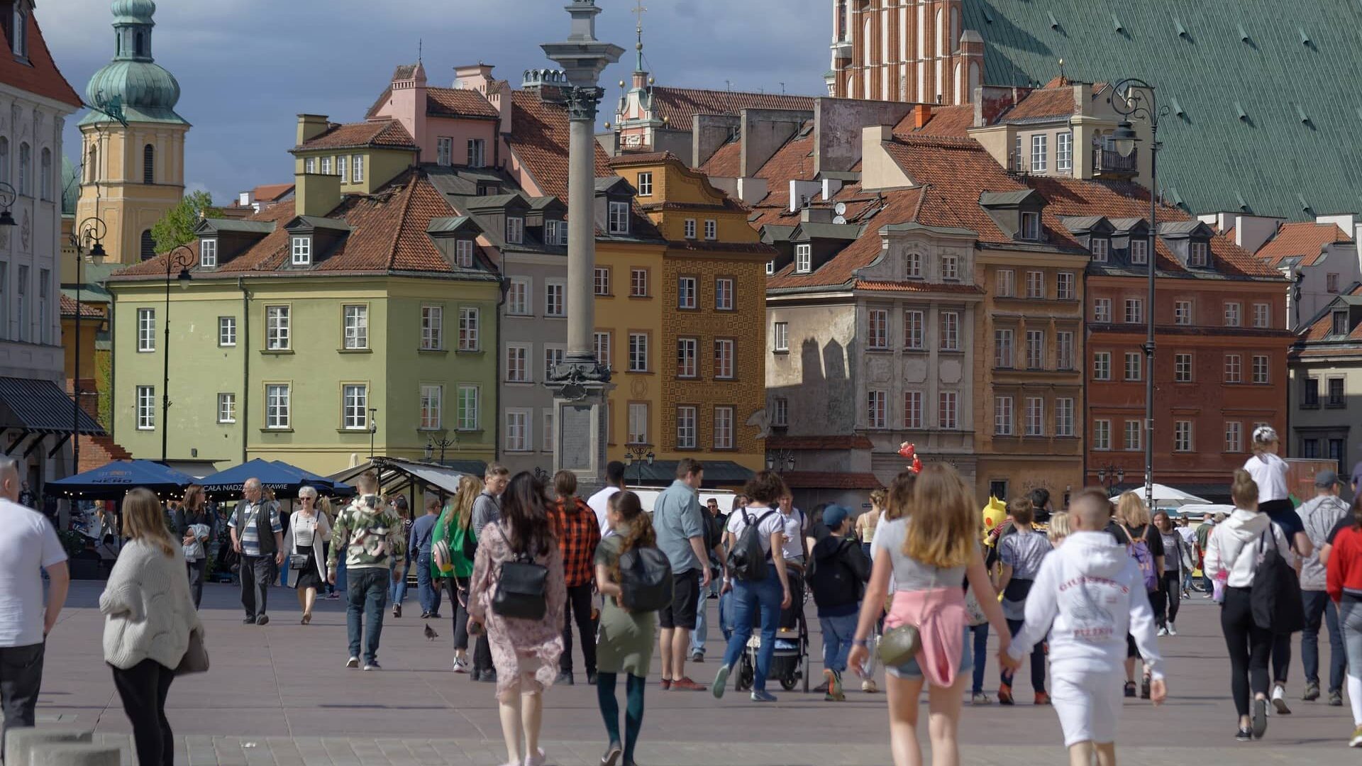 Zdjęcie przedstawia starówkę w Warszawie i spacerujących ludzi.